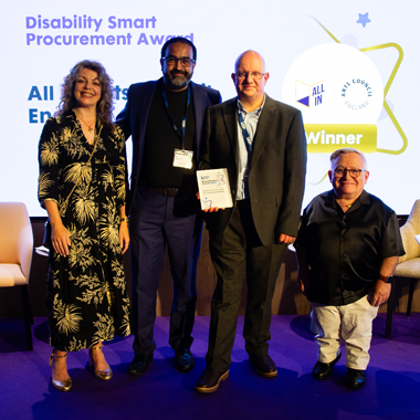 Colleagues Abid Hussain and Roger Dennis represent All In and Arts Council England as they collect the Disability Smart Procurement award on a purple, backlit stage at the Disability Smart Awards 2025. On either side, they’re joined by Diane Lightfoot, CEO Business Disability Forum, and Simon Minty, ambassador of Business Disability Forum.